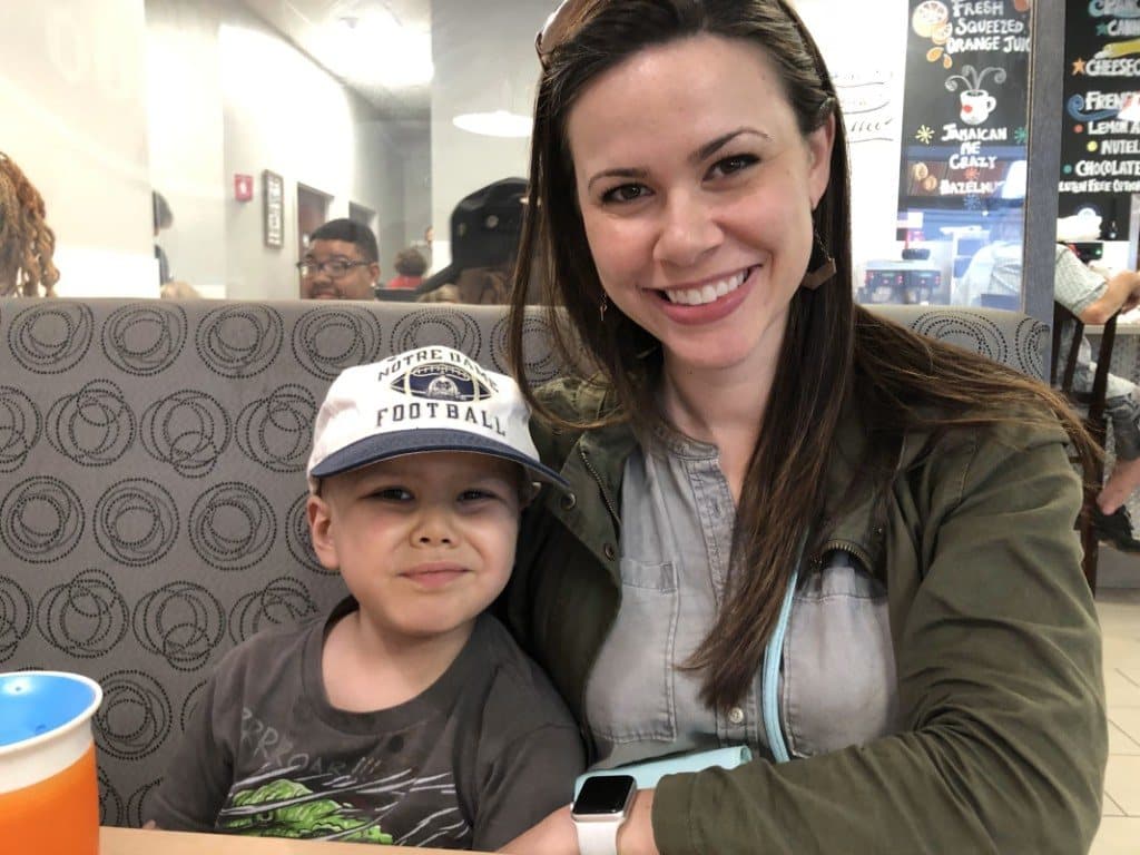 Jacob in a Notre Dame football cap sits close beside his mom, who is smiling, in a restaurant booth.