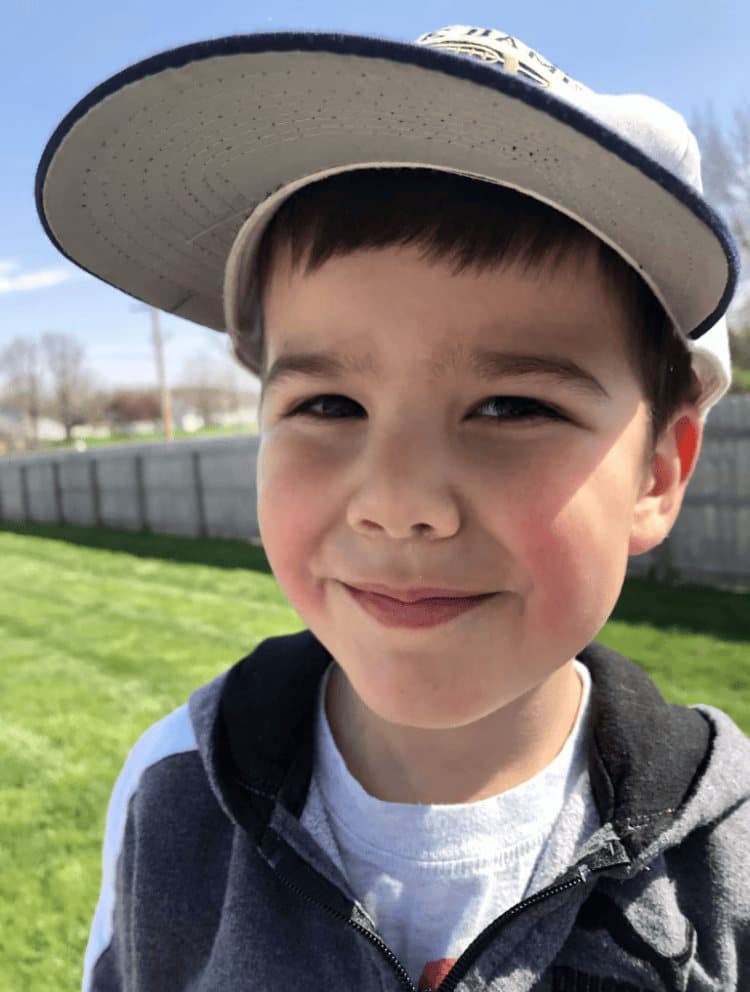Jacob smiling outdoors in a baseball cap, sunlight on his face and green grass behind him.